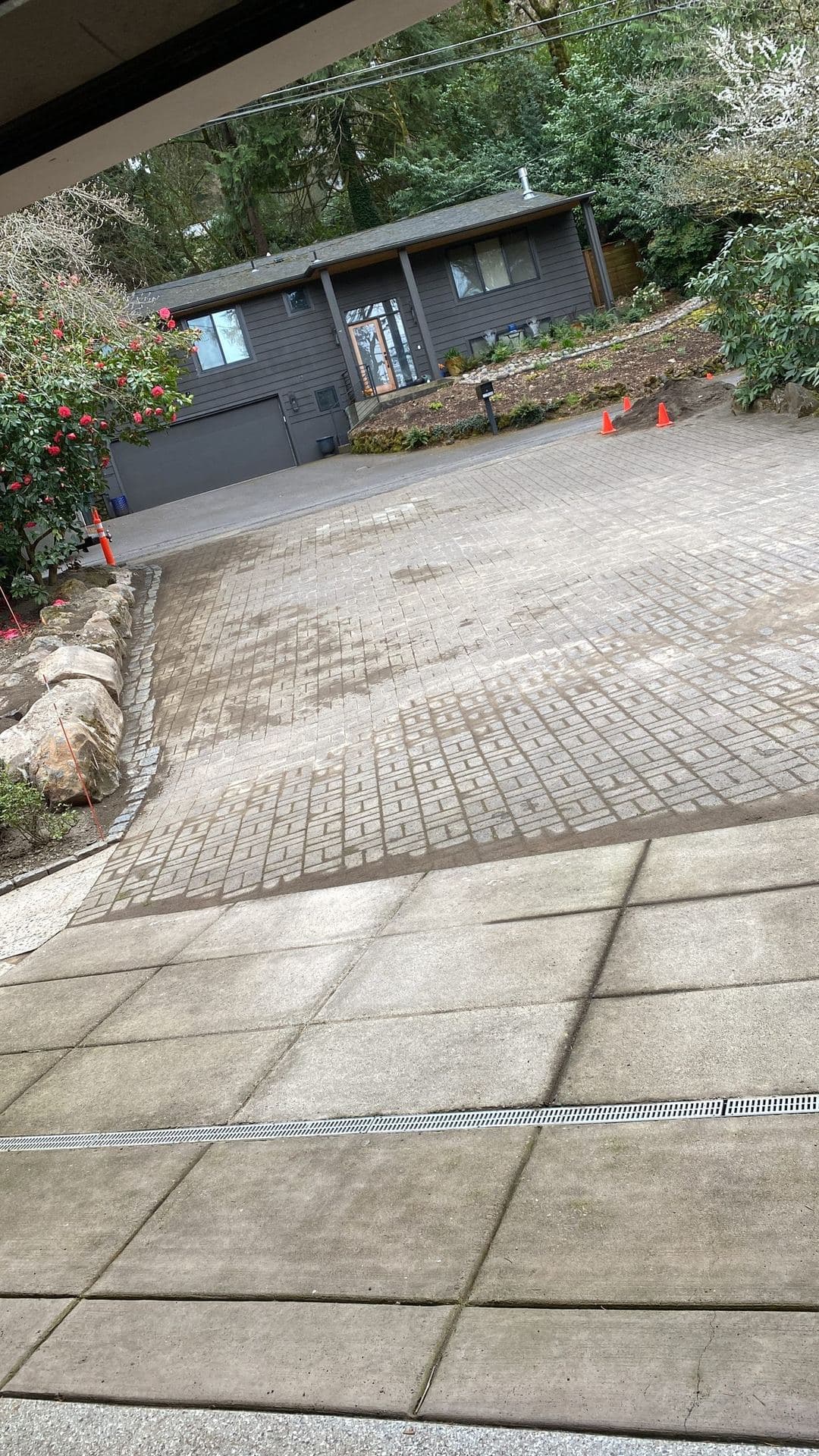 Finished stamped concrete driveway with a channel drain in front of a gray-sided home