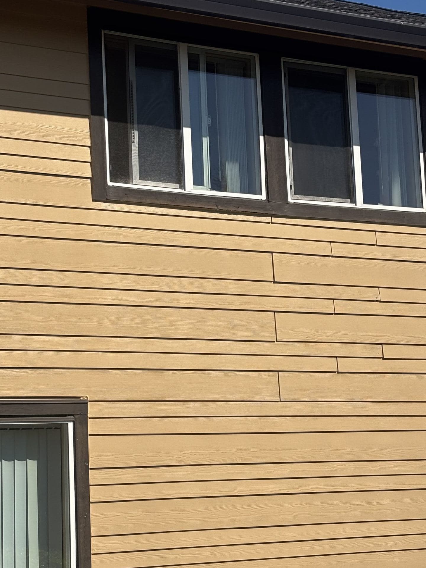 Close view of finished lap siding with white-framed sliding windows and dark trim