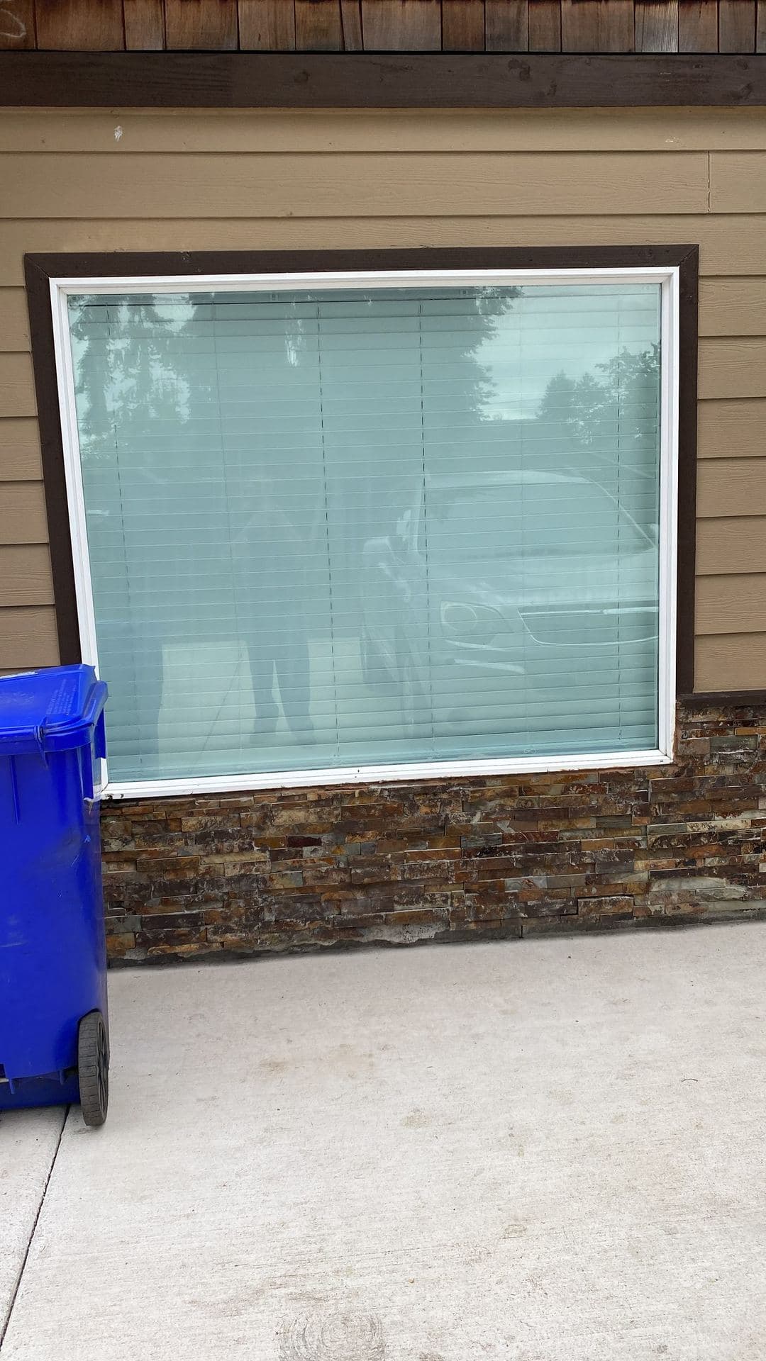 Finished picture window with white frame and dark trim above stone veneer