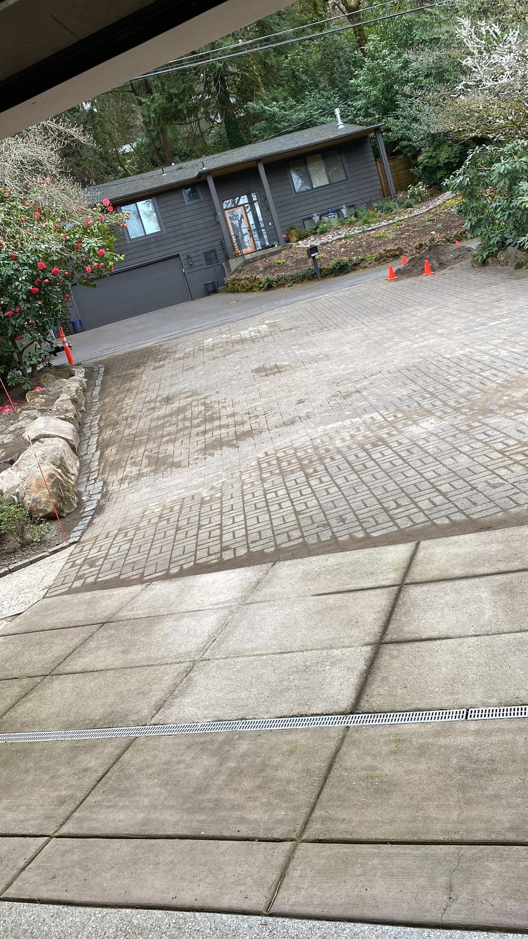 Finished stamped concrete driveway with a channel drain in front of a gray-sided home